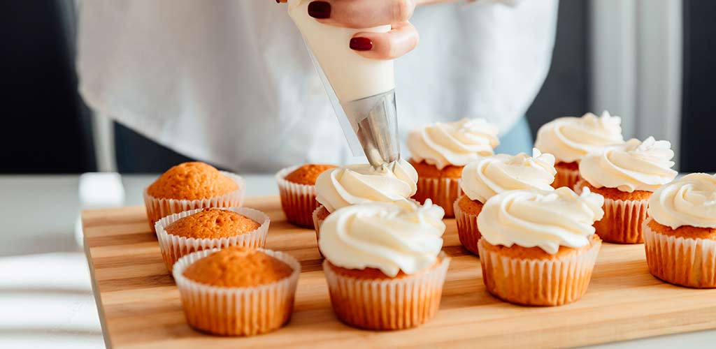 Woman decorates freshly baked cupcakes with cream